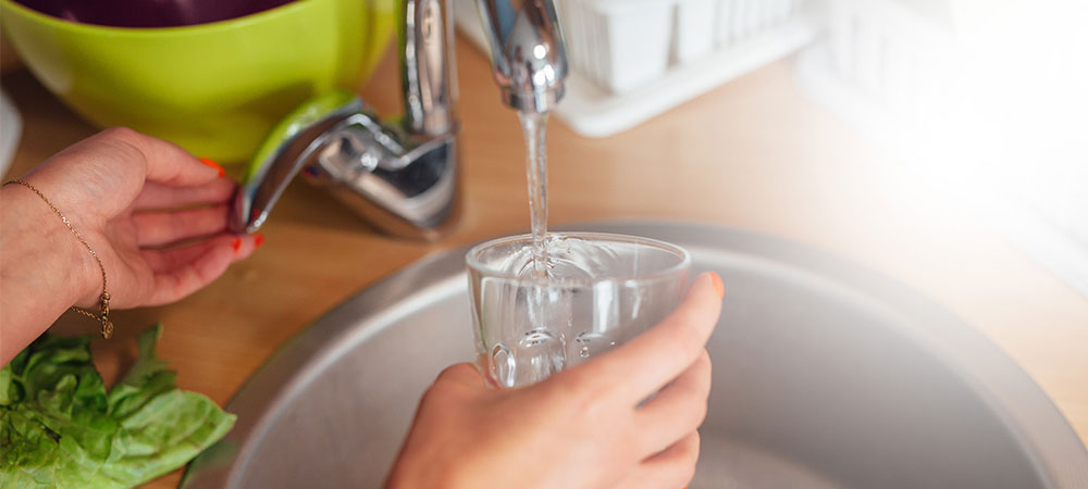 Person filling a glass with water from the tap